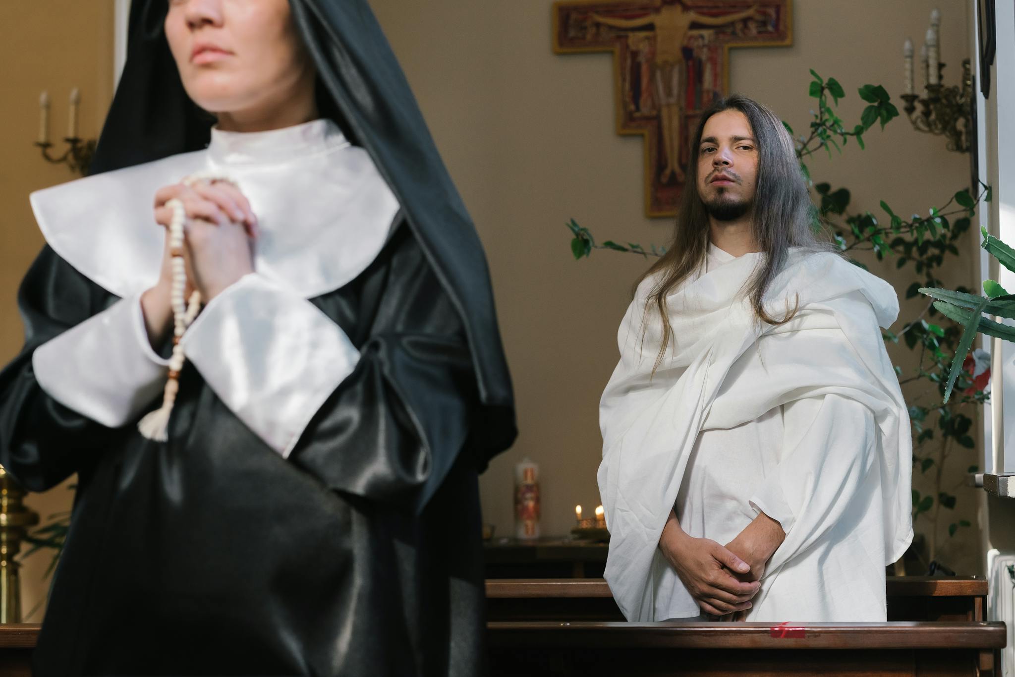 A nun in prayer beside a figure in white, in a church setting.
