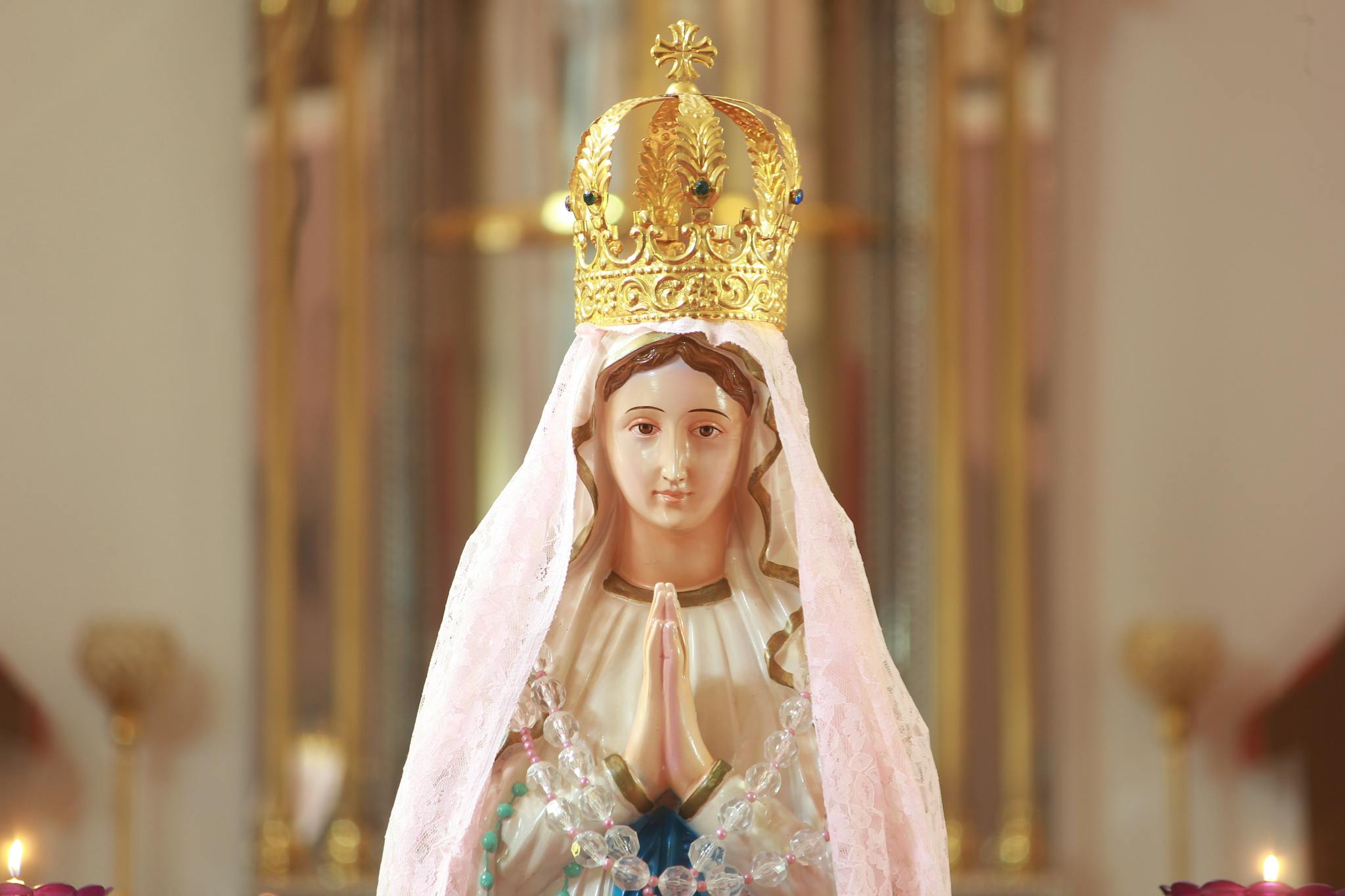 Close-up of a statue of Our Lady of Fatima with crown and prayer beads, inside a church.