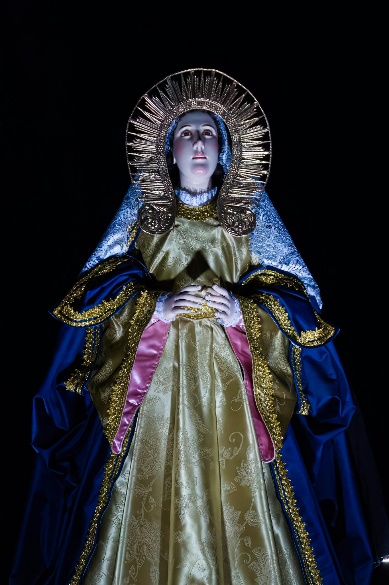 Illuminated Virgin Mary statue with halo, captured against a dark background, ornamented with intricate details.