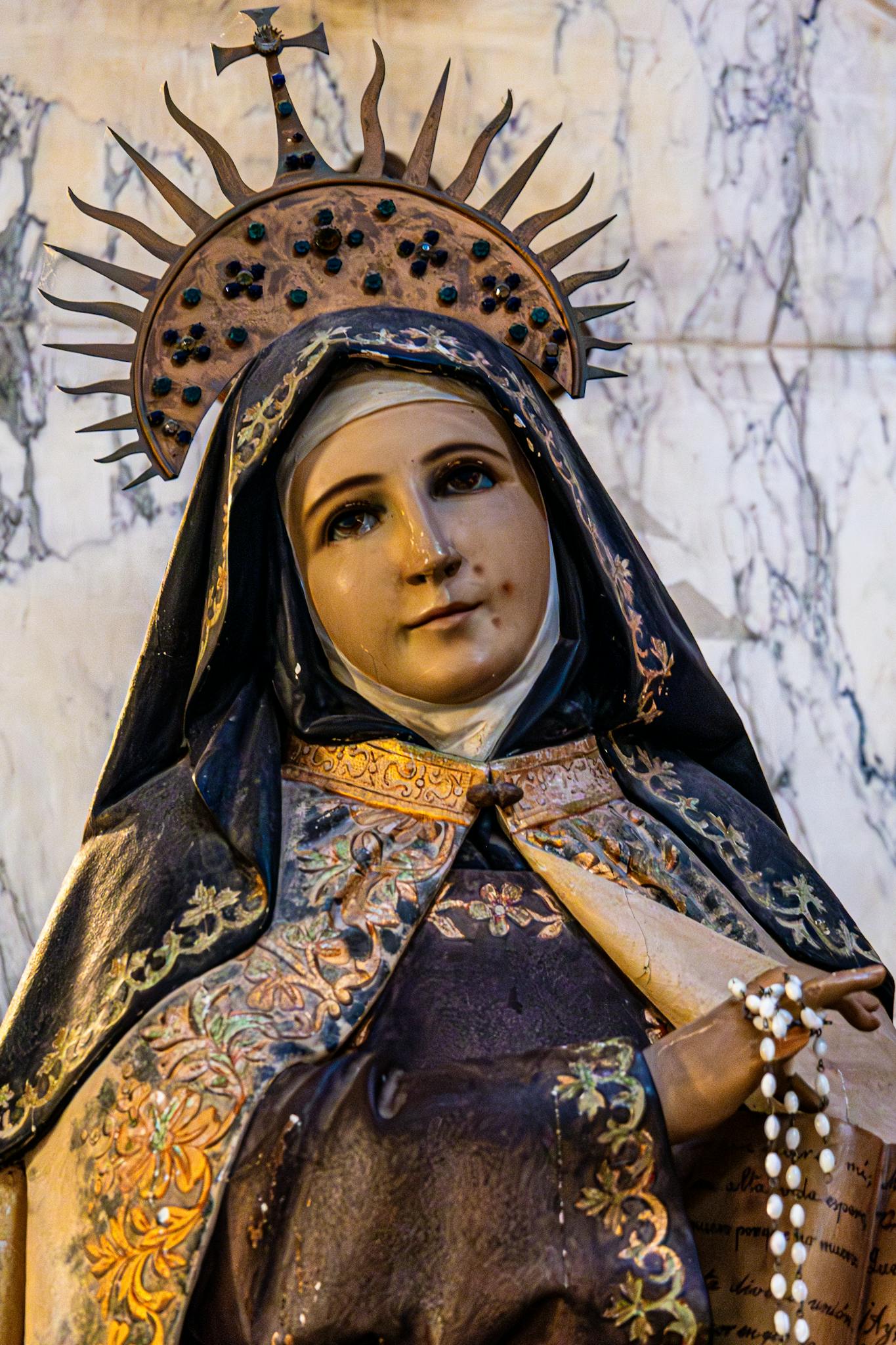 Ornate statue of a saint holding prayer beads in a historic church setting.